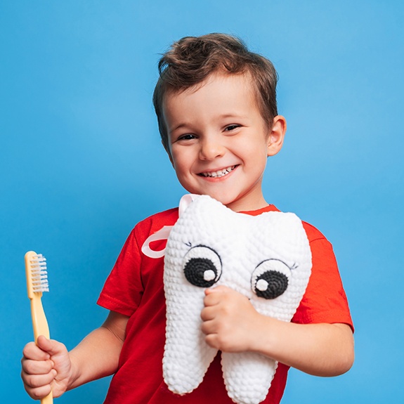 Happy little boy holding a toothbrush and stuffed tooth