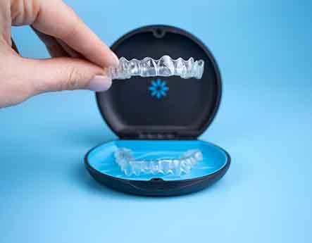 A hand holding an Invisalign tray over its carrying case