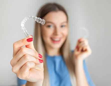 A woman with a non-blurred Invisalign tray in one hand and a blurred one in the other