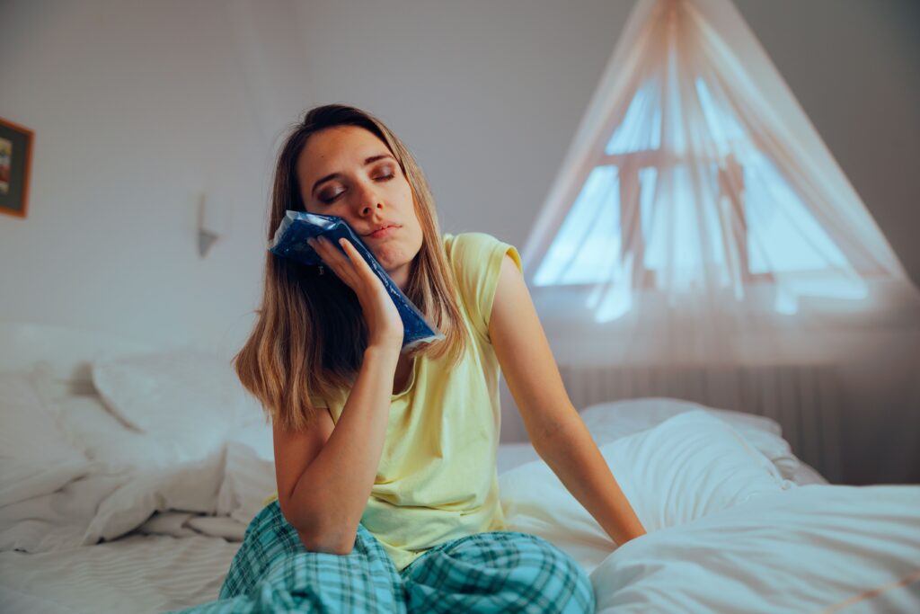 A woman sitting in bed holding an ice pack to her jaw after wisdom teeth removal surgery.