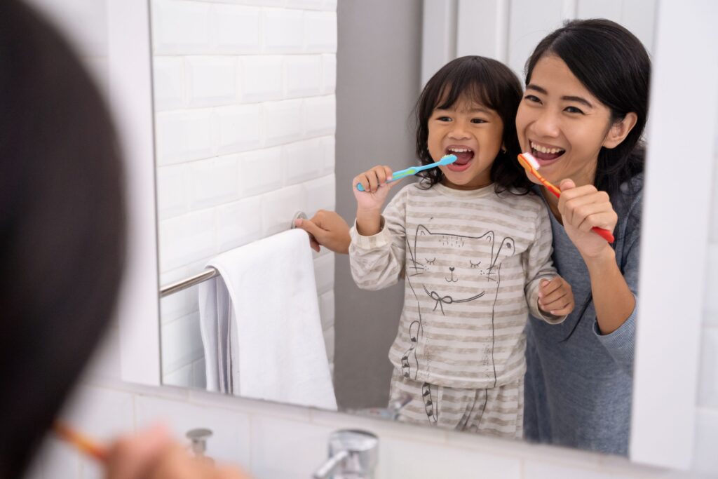 Woman and girl at bathroom mirror brushing teeth together